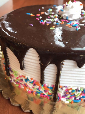 This ice cream cake will be the highlight of any birthday party as it combines enthusiasm with simplicity. Vanilla whipped cream is dressed in a glaze of chocolate fudge and brought to life with a colorful display of rainbow sprinkles around the base of the cake.