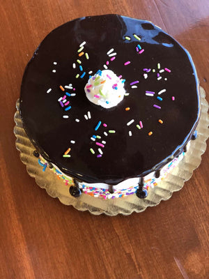 This ice cream cake will be the highlight of any birthday party as it combines enthusiasm with simplicity. Vanilla whipped cream is dressed in a glaze of chocolate fudge and brought to life with a colorful display of rainbow sprinkles around the base of the cake.